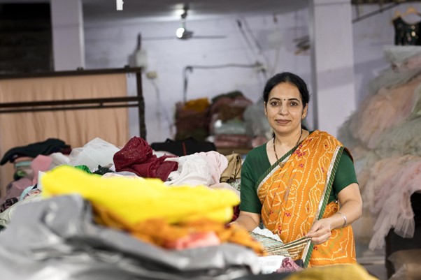 Transforming Fashion - a woman worker in the fashion industry poses with piles of clothes